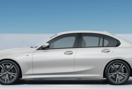 Side view of a white four-door sedan with alloy wheels parked on a light surface against a blue sky.