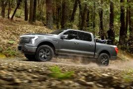 Gray pickup truck driving fast on a dirt road through a forest, kicking up dust in the woods.