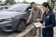 Man points at a car's front wheel while a uniformed woman records details on a tablet beside him on the curb.