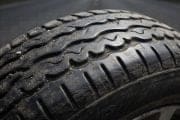 Close-up of a car tire tread with visible dirt and wear on a road surface behind it.