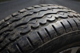 Close-up of a car tire tread with visible dirt and wear on a road surface behind it.