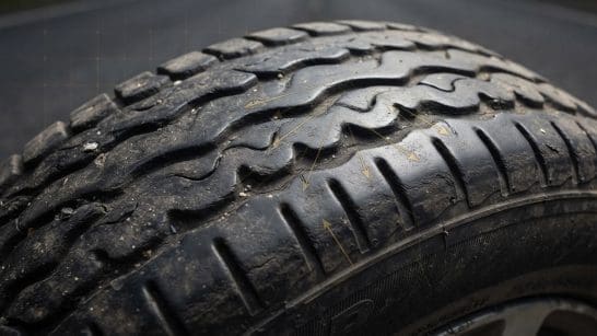 Close-up of a car tire tread with visible dirt and wear on a road surface behind it.