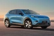 Blue electric SUV shown in a three-quarter front view parked on a flat desert at sunset, facing left.