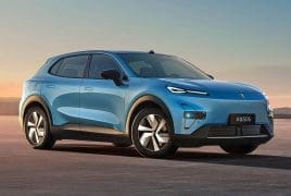 Blue electric SUV shown in a three-quarter front view parked on a flat desert at sunset, facing left.