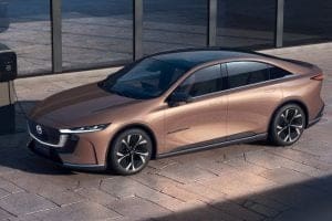 Bronze-colored Mercedes-Benz sedan parked on a paved lot beside a charging station.