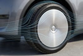 Close-up of a car wheel with a silver aerodynamic hubcap and blue airflow lines illustrating reduced air resistance around the tire.