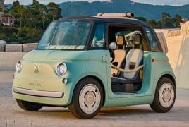 Mint green vintage Fiat 500 with the driver's door open, parked on a stone plaza with hills in the background.