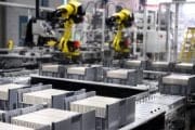 Automated factory line with yellow robotic arms assembling rectangular components on a conveyor belt.