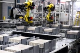 Automated factory line with yellow robotic arms assembling rectangular components on a conveyor belt.