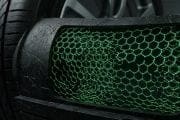 Close-up of a car's front grille with a green honeycomb mesh and a tire in the background, focusing on texture.