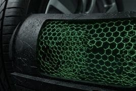 Close-up of a car's front grille with a green honeycomb mesh and a tire in the background, focusing on texture.