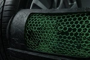 Close-up of a car's front grille with a green honeycomb mesh and a tire in the background, focusing on texture.