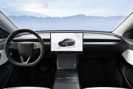 Front-seat view of a modern car interior with a large central touchscreen displaying a car image, a round steering wheel, and a mountain landscape visible through the windshield.