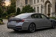 Grey BMW sedan plugged in to charge on a cobblestone driveway in front of a historic estate and gardens.