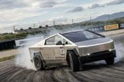 Tesla performance race car drifting on a racetrack, tire smoke rising, number 01 visible with track barriers in the background