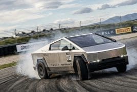 Tesla performance race car drifting on a racetrack, tire smoke rising, number 01 visible with track barriers in the background