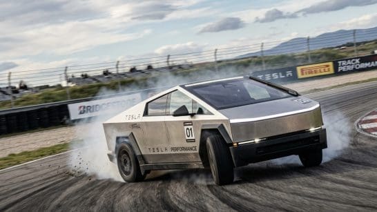 Tesla performance race car drifting on a racetrack, tire smoke rising, number 01 visible with track barriers in the background