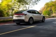 Rear three-quarter view of a silver electric car driving on a tree-lined road during daytime (fall foliage).