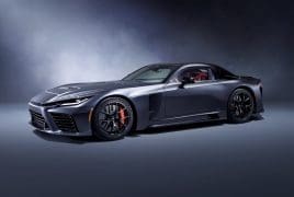 Sleek dark gray sports car with red interior parked in a studio, low stance and bold front grille visible.