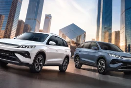 Two BYD SUVs parked in a modern city plaza, white and blue models with glass skyscrapers in the background.