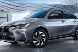 Front three-quarter view of a silver Toyota Yaris Ativ HEV Premium sedan in a modern concrete setting with sleek lines and alloy wheels.