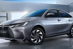 Front three-quarter view of a silver Toyota Yaris Ativ HEV Premium sedan in a modern concrete setting with sleek lines and alloy wheels.